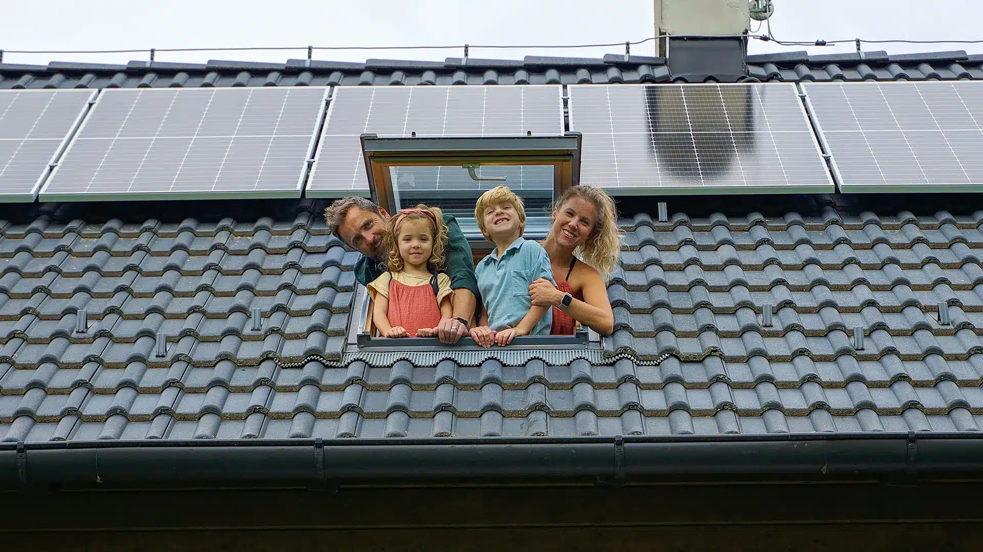 Famille heureuse à la fenêtre de toit et vue sur la toiture équipée de panneaux solaires photovoltaïques